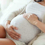 ALL Pregnant Travelers Need THIS For U.S Entry! Pregnant woman holding her belly, sitting comfortably.