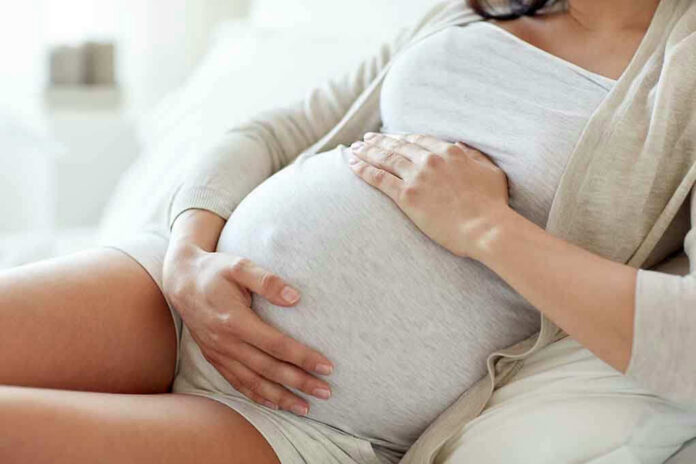 564114571 Pregnant woman holding her belly, sitting comfortably.