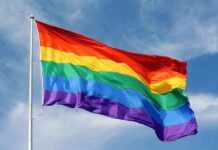 A rainbow flag waving against a blue sky
