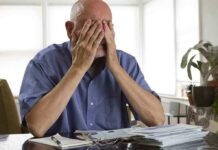 Election Heist Exposed: Fake GOP Guides Flooded Mailboxes Elderly man sitting at a table with his hands covering his face, surrounded by paperwork