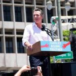 ICE Raids Newsom Press Conference Man speaking at a rally podium outdoors