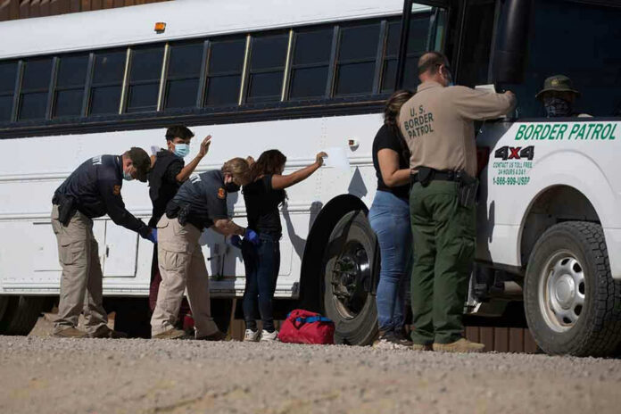 1973414852 Border patrol officers investigating people near a bus.