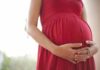 Pregnant woman in a red dress holding her belly