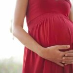 Pregnant woman in a red dress holding her belly