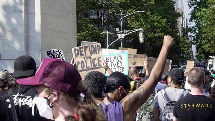 shutterstock_1754395223 crowd at a protest holding signs and raising fists