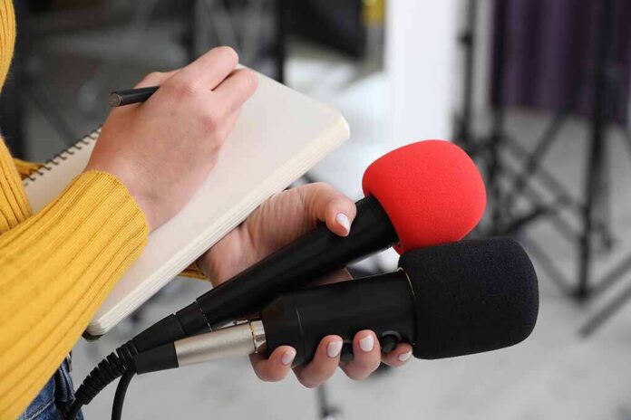 Journalist holding two microphones while writing in a notebook