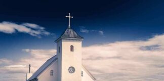 White countryside church with steeple and cross under a dramatic sky