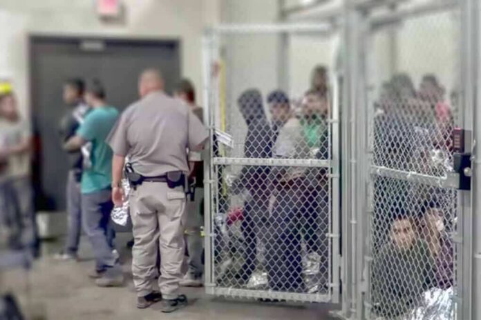 shutterstock_1229072188 Detention facility with people behind chain-link fence and officer nearby