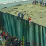Germany DEMANDS Country Take Back It’s Migrants! People climbing a tall beachside border fence