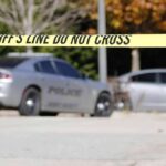 Sheriff's line tape blocking a street with police cars behind