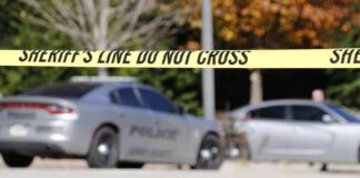 Sheriff's line tape blocking a street with police cars behind