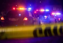 Hobo’s Brawl Turns GUT-WRENCHING! Police cars with flashing lights behind yellow caution tape at night