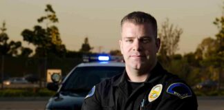 Police officer standing with arms crossed in front of patrol car