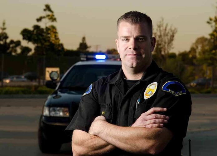 Police officer standing with arms crossed in front of patrol car