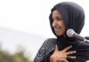 Ilhan Omar speaking at a microphone with hand on chest