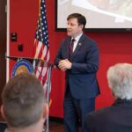 Vanished Congressman RETURNS – Reveals Where He’s Been Speaker in a navy suit addressing an audience at a podium
