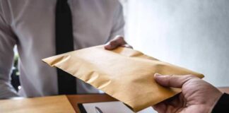 Hands exchanging a brown envelope across a desk