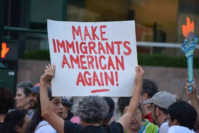 shutterstock_1449371015 Teddy Williams at a protest holding a sign reading 'Make Immigrants American Again'