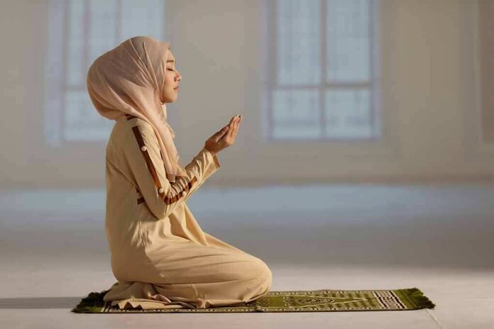 Woman in hijab praying on a mat indoors