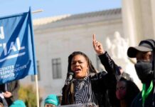 Woman speaking at a rally with raised finger and microphone