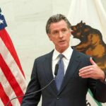 Gavin Newsom speaks at a podium with U.S. and California flags behind him