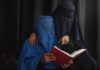 Two veiled women reading a red book together