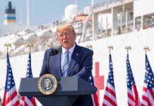 Trump Terminates Biden’s Mandate, Says He can Do It CHEAPER Donald Trump speaking at a podium with American flags and a ship in the background