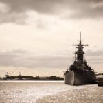 Battleship moored at a harbor under cloudy sky