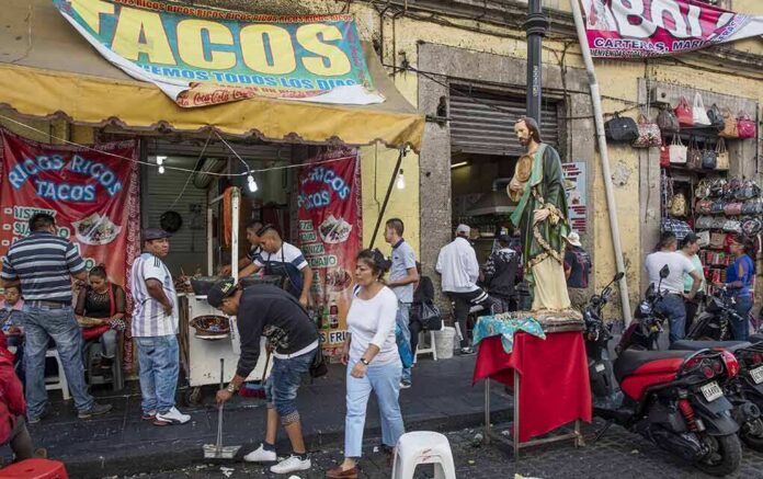 Street taco stand with people and a religious statue on a sidewalk