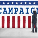 Trump’s CEO Buddy Triumphs In Primaries! Man in suit writing on large campaign banner with stars and stripes