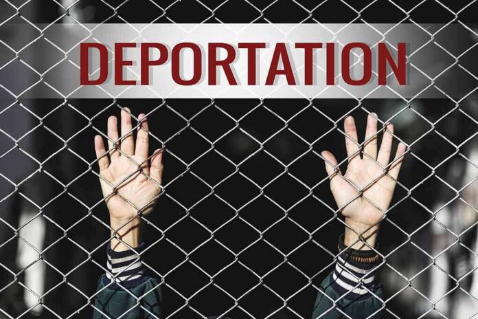 shutterstock_519187753 Hands gripping chain-link fence with deportation sign