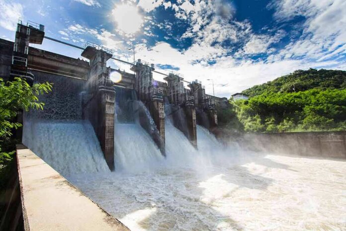 shutterstock_541668826 Hydroelectric dam spillway releasing water under bright sky