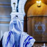 El-Sayed’s ‘Lesbian Rosh Hashanah’ Plan BACKFIRES Spectacularly Person in white and blue prayer shawl facing ornate interior