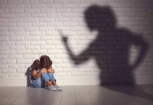 Child sitting against wall with shadow of an adult pointing