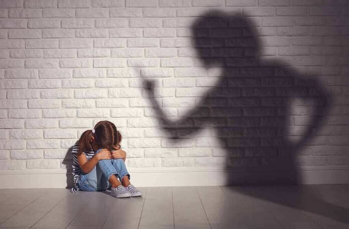 shutterstock_1017359518 Child sitting against wall with shadow of an adult pointing