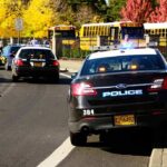 Police cars with flashing lights near school buses on a city street