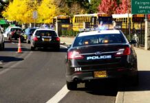 Teen Faces TERRORISM Charges After Cafeteria Poisoning Police cars with flashing lights near school buses on a city street