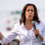Even Kamala’s Husband Doesn’t Want Her To Run Again woman speaking into a microphone at an outdoor event