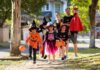 Children in Halloween costumes trick-or-treating with adults on a sunny street