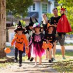 Children in Halloween costumes trick-or-treating with adults on a sunny street