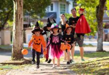 Children in Halloween costumes trick-or-treating with adults on a sunny street