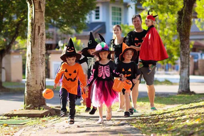 shutterstock_1499421917 Children in Halloween costumes trick-or-treating with adults on a sunny street