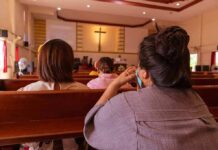 Giant Crucifix Fatally Crushes Priest During Mass people seated in church pews facing a cross