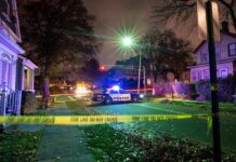 Homecoming Horror: 2 Dead, 35 Hit Police car blocks residential street at night behind caution tape
