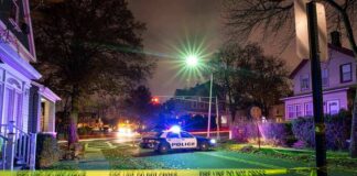Police car blocks residential street at night behind caution tape