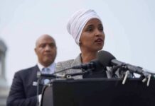 Ilhan Omar speaking at a podium with André Carson standing behind