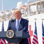 Judge Throws Wrench Into Trump’s $20 Million Ad Blitz Ahead of Midterms Donald Trump speaking at a podium with American flags and a ship in the background