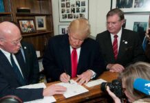 Donald Trump signs a document as Corey Lewandowski looks on amid officials and press