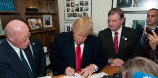Donald Trump signs a document as Corey Lewandowski looks on amid officials and press