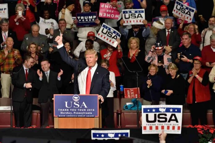 shutterstock_538492747-1 Donald Trump addresses a rally crowd at a podium, raising his fist